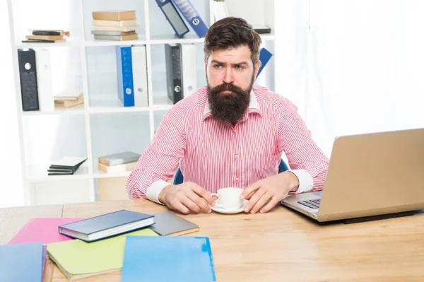 Brutal hipster with serious look drink coffee at agent desktop in modern office, employee — Stock Photo, Image
