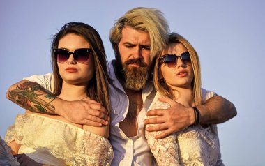 Yaz tatili. İlişkiler dostluk romantizmi. Üçlü konsept. İkisine de aşığım. Çatıdaki partiden arkadaşlar. Havalı hipster ve kadın beyaz elbiseler. Kadınlar ve erkek arkadaşlar sarılıyor. Aile