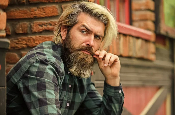 Depressed bearded man checkered shirt. Hipster dyed hair and beard. Man casual fashion. Hipster in sunglasses. Hairdresser and barbershop. Brutal male with blond hair irish architecture background