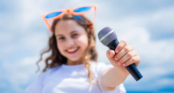 Teen girl singing song in microphone on sky background, karaoke music — Stock Photo, Image