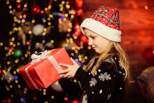 Meisje schattig kind houden verpakt cadeau in de buurt van kerstboom. Winter winkelen. Feestje dat eigenlijk leuk klinkt. Vrolijk kerstfeest. Een schattig kind draagt kerstmuts om kerst te vieren. Kerstcadeau kopen — Stockfoto