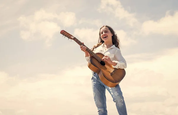 little girl play guitar she loves music. music school classes. small guitar player on sky background. country music style. string musical instrument. play on acoustic guitar