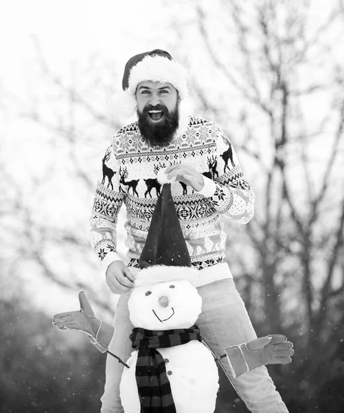 休息だ。冬の活動。クリスマスだ。サンタの帽子は雪で遊ぶ。冬休みの屋外。寒い日の暖かいセーター。髭の男が雪だるまを作る。ハッピーヒップスターxmasを祝う準備ができて — ストック写真