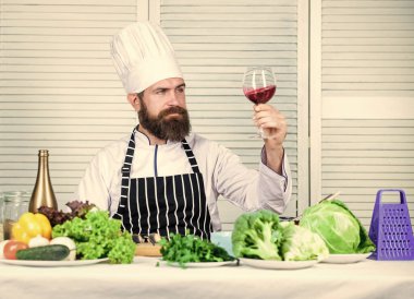 Usta şef bir bardak şarap tutuyor. Biraz alkol ekle. Yemekte hangi şarap servis ediyor? Şarap arıtma. Mutfak konsepti. Şarap ve yemeği uzman gibi eşleştir. Erkekler şapka takar ve önlük giyer.