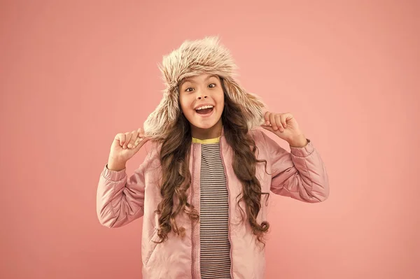 Warme glimlach. gelukkig kind roze achtergrond. warme kleding voor het koude seizoen. Kindermode. trendy meisje ziet eruit als hipster. herfst stijl. Jeugdactiviteit. bont oorflap hoed accessoire. klein meisje winter hoed — Stockfoto