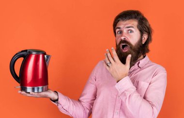 Vay canına. Bıyıklı ve sakallı vahşi bir adam. Elektrikli ev aleti. Sakallı adam kırmızı elektrikli su ısıtıcısı kullanıyor. Erkek ev idaresi konsepti. Sıcak suya ihtiyacım var. Adam çay ya da kahve içecek.