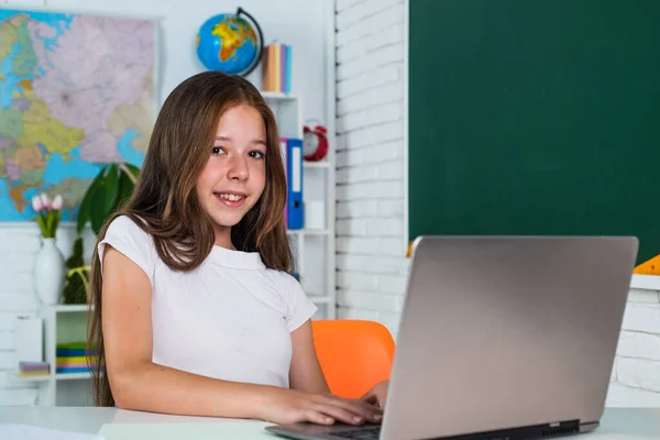 现代教育。知识日。小学生们坐在桌旁用电脑。女孩是大学生。回学校去十几岁的女孩带着笔记本电脑在教室里工作。快乐的孩子在网上学习 — 图库照片