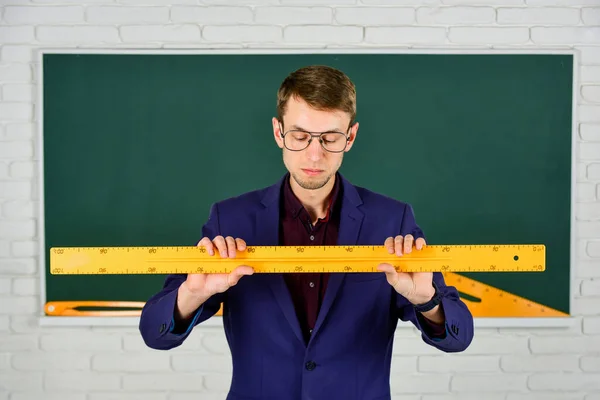 Teacher man at chalkboard holding ruler, math subject concept