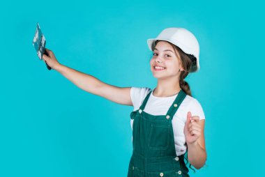 Kendine güvenen çocuk spatulayı tamir ederken kullanır. İnşaat ve yenileme konsepti. Mutlu kız spatula aleti kullanır. Genç müteahhit güvenlik kaskı takıyor. Koruyucu şapkalı genç işçi