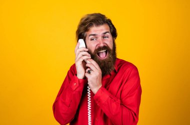 İletişim. Sakallı adam kırmızı gömlek giyer. Sıradan bir erkek telefonu. Sohbet konsepti. Adam sekreter ya da asistan retro telefonda konuşuyor. Telefonlu acımasız adam.