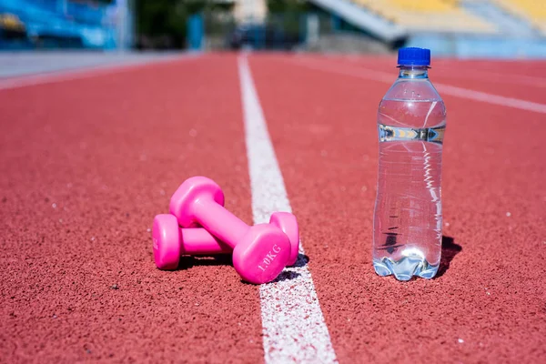 sport tool and equipment. dumbbells on racetrack in stadium. hydration after fitness. healthy lifestyle. water balance in body while workout. barbells and bottle on running track