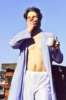 Mavi çizgili pijamalı, elinde fincanla beyaz maço.