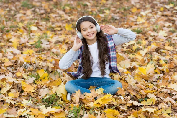 Bambino felice in stile casual trascorrere del tempo nella foresta autunnale con foglie d'acero godendo del bel tempo durante l'ascolto di musica in cuffia, vita moderna — Foto Stock