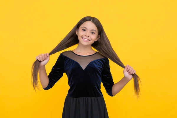 Criança pequena feliz com beleza olhar sorriso segurando longo cabelo morena no vestido de moda fundo amarelo, salão — Fotografia de Stock