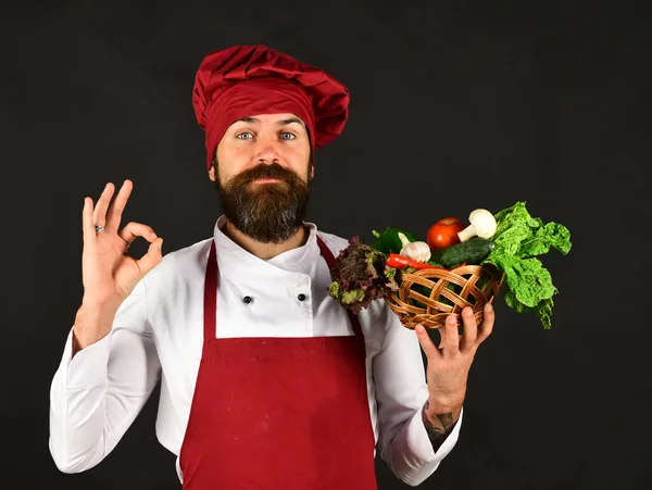 Koch mit ernstem Gesicht in weinroter Uniform hält Gemüse in der Hand — Stockfoto