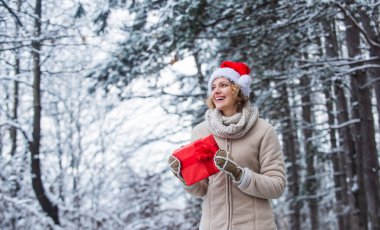 Kadın sıcak giysileri, karlı orman. Doğa karla kaplı. Kış kıyafeti. Yeni yıl. Mutlu noeller. Boks günü. Kızda kırmızı hediye paketi var. Kış tatili konsepti. Kış hediyesi. Noel 'i kutlayın.