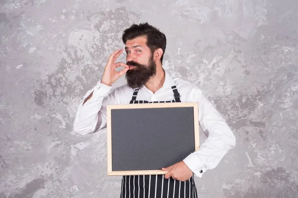 Cocinero masculino hipster caucásico con mirada satisfecha mostrando gesto de perfección sosteniendo pizarra vacía publicidad clase magistral escuela culinaria, gusto perfecto —  Fotos de Stock