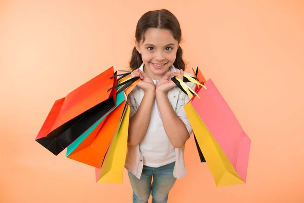 Módní expert. Dítě roztomilé nakupování expert pomáhá nést balíčky při nakupování. Malý obchod expert. Dívka shopaholic nemá rád nakupování. Kluk holka šťastný obličej nese parta balíčky žluté pozadí — Stock fotografie