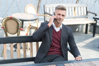 Resmi tarz konuşma işinde yakışıklı bir yönetici cep telefonu iletişiminde açık kafede dinleniyor, konuşuyor.