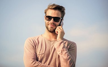Hoş sohbetti. Kendine güvenen bir adam telefonda konuşur. Arkadaşına seslen. Maço adam cep telefonu kullanıyor. Hayattaki modern teknoloji. Her zaman görüşüyoruz. Seksi erkek gökyüzü arka planı. Sıradan bir adam. Moda modeli