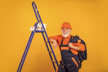 Isı yalıtımı işe yarıyor. Boyacı merdiveni. Onarım yapmak için. İş elbiseli bir adam boş odaya duvar boyuyor. Boyalı kovayla şapkalı bir ressam. İnşaat işçisi boyama cephesi