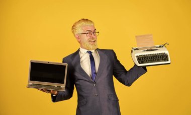 Dizüstü bilgisayara karşı daktilo. İş adamı modern teknolojiyi kullanır. Adam sakalını sarıya boyamış. Yeni modern aletler al. Yararlı bir cihaz. Modern yerine modası geçmiş. Vintage değerleri uzmanı