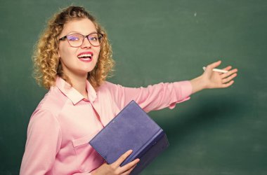 Pedagog kitabı tutuyor ve bilgiyi açıklıyor. Eğitim konsepti. Öğretmen zor konuyu açıkla. Karatahtanın önündeki kadın öğretmen. Öğrencilerin en iyi öğretmeni. Bilgiye karşı tutkulu