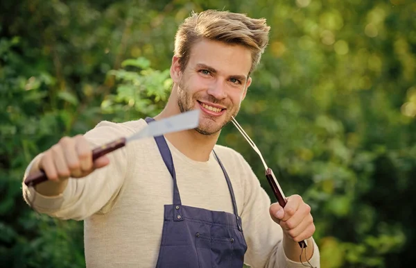 Cucinare hamburger. L'uomo tiene attrezzature per barbecue. Cibo grigliato. Utensili da barbecue. Weekend estivo. Strumenti per arrostire carne all'aperto. Festa al barbecue. Concetto picnic. Bbq chef. Bello ragazzo cucina cibo — Foto Stock