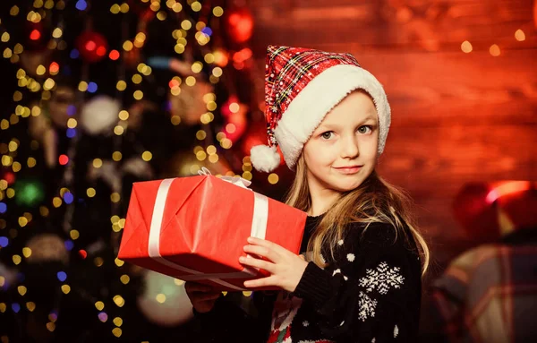 Feestje dat eigenlijk leuk klinkt. Vrolijk kerstfeest. Een schattig kind draagt kerstmuts om kerst te vieren. Winter winkelen. Koop kerstcadeau. Meisje schattig kind houden verpakt cadeau in de buurt van kerstboom — Stockfoto