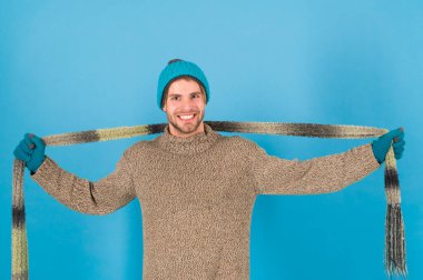 Sıcak eşarpla serin günleri ısıt. Mutlu adam uzun atkı takıyor. Yakışıklı adam elinde eşarpla gülümsüyor. Kış için moda aksesuar. Çizgili desenli şık örgü eşarp