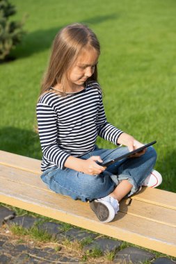 Tecrübe öğrenme ve oynama şeklini değiştirir. Küçük çocuk park bankında otururken tablet kullanıyor. Mobil teknoloji. Modern hayat. Yeni teknoloji. Çevrimiçi okul ve evde eğitim. Uzaklık eğitimi