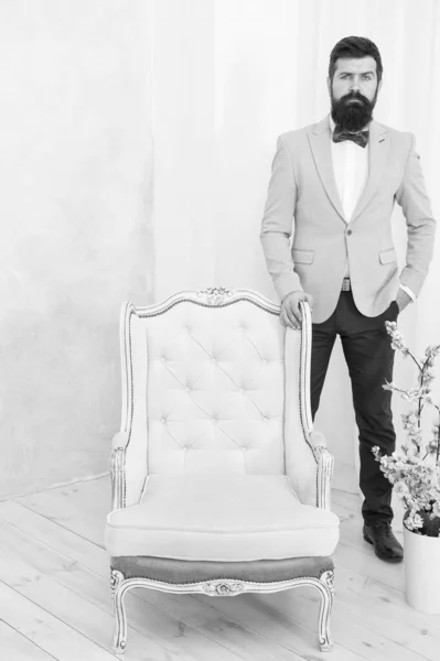 awaiting her at chair. professional interior designer. bride groom on wedding day. event host wear bow tie. adult hipster man in stylish tuxedo. male fashion and beauty. unshaven man at luxury chair