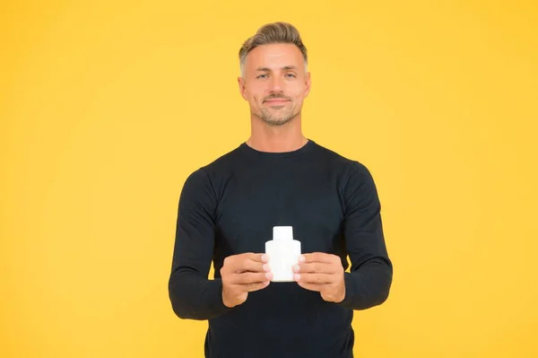 Hombre caucásico guapo con la piel de la cara sin afeitar y el pelo elegante en estilo casual celebrar perfume botella fondo amarillo, cuidado de la piel —  Fotos de Stock