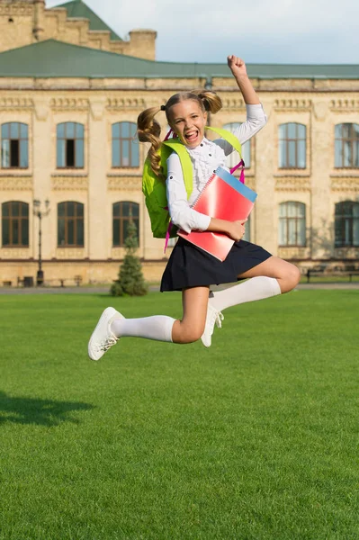 Енергійний дитина в формальній формі з навчальними книгами рюкзак стрибок у шкільному дворі щасливе святкування, назад до школи — стокове фото