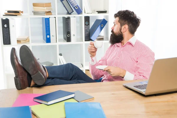 Barbudo hombre con mirada brutal relajarse en el escritorio beber café en la oficina moderna, hipster —  Fotos de Stock