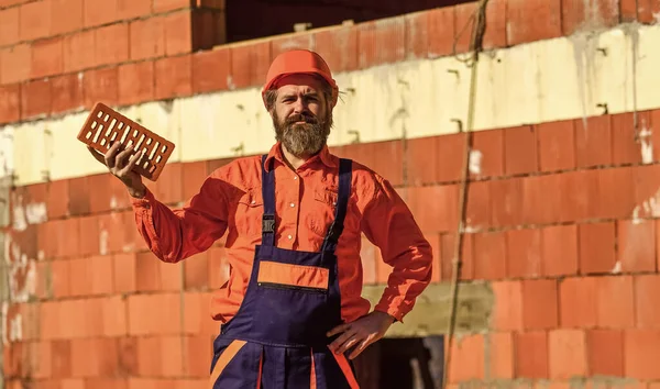 Builder hold brick. Bearded man wear hard hat at construction site. Brick building material used to make walls. Lightweight brick made from expanded clay aggregate. Element in masonry construction — Stock Image Builder hold brick. Bearded man wear hard hat at construction site. Brick building material used to make walls. Lightweight brick made from expanded clay aggregate. Element in masonry construction Royalty Free Stock Images