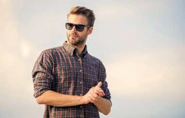 Erkek gözlüklü model açık havada mavi gökyüzü arka planı. Yakışıklı adam güneş gözlüğü takıyor. Mükemmel görüş. Göz sağlığı. Modaya uygun güneş gözlükleri. Moda güneş gözlüklü hippi. Ultraviyole koruma kavramı