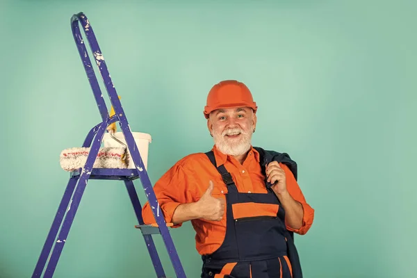 Reparieren. Seniormaler benutzt Rolle auf Leiter. Malerei der Wand in blau. professioneller Maler in Arbeitskleidung. Arbeiter streichen Wand in Raum. männliche Dekorateur Malerei mit Walze — Stockfoto