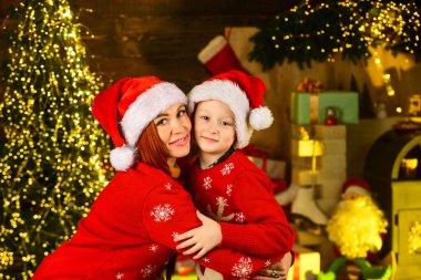 Anne ve oğlu Noel 'i kutluyor. Aile tatili zamanı. Küçük çocuk annesini seviyor. Noel partisi zamanı. Anne ve çocuk Noel Baba şapkası ve kazak giyiyor. Hediyeleri ve hediyeleri akrabalarınızla paylaşın
