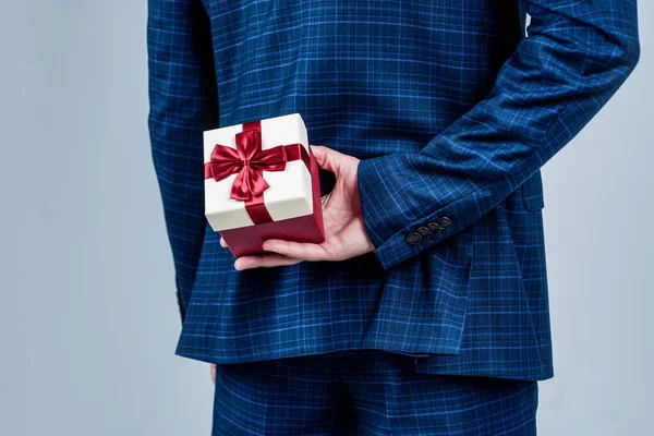 Caja de regalo atada con lazo de cinta roja sostenida en mano masculina detrás de la espalda en traje de moda de estilo formal, presente — Foto de Stock