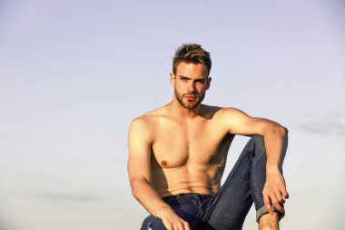 Dinlenme zamanı. Sporcunun seksi bir vücudu var. Gün batımında kaslı bir adam. Maço adamın çıplak gövdesi var. Kot pantolon giymiş seksi bir adam. Gökyüzü arka planında erkek manken. Yaz, dışarıda dinlenme.