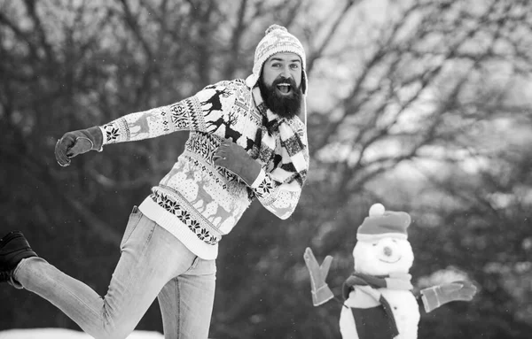 Ha en rolig vinterdag. Låt det snöa. Julhelgen. Aktiv livsstil. Snö spel. Fritid på frisk luft. Man glad skäggig hipster stickad hatt och varma handskar leka med snögubbe snö utomhus — Stockfoto