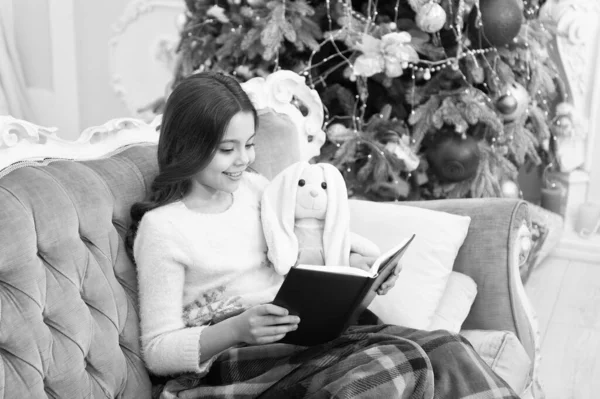 Просто хочу почитать по-зимнему. Очаровательная маленькая девочка читала Рождественскую историю игрушечному другу. Happy little child read book by xmas tree. Должен читать список во время каникул — стоковое фото