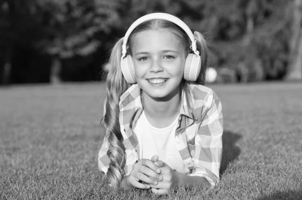 Nuova tecnologia per i bambini. ricordi d'infanzia felici. ascoltare musica. Torniamo a scuola. studio dei bambini nel parco. rilassarsi sull'erba verde in cuffia. piccola ragazza ascoltare audiolibro — Foto Stock