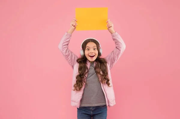 Gelukkig tiener meisje luisteren muziek in hoofdtelefoon presenteren leeg papier, terug naar school — Stockfoto