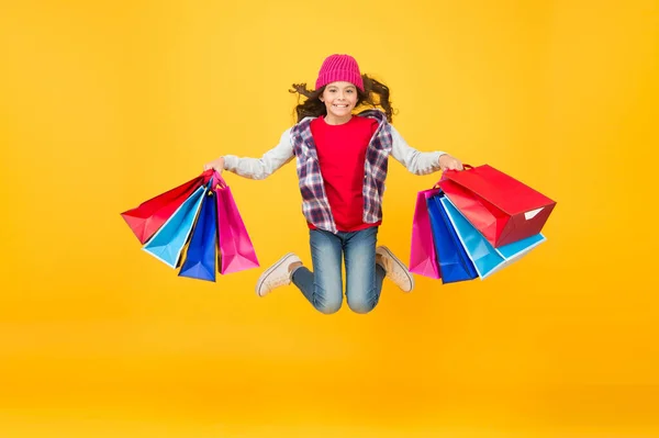 快乐的小女孩带着购物袋跳黄色背景，打折 — 图库照片