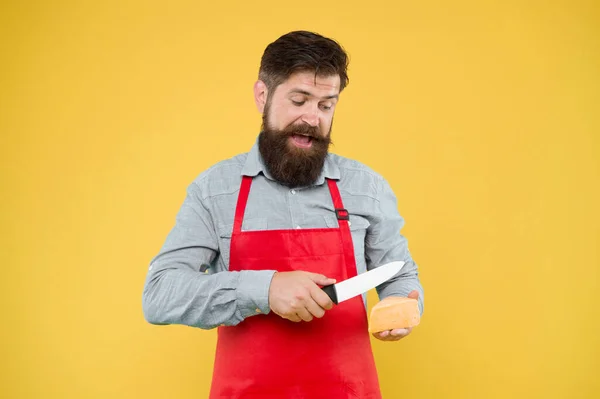 Professionellt kök koncept. Ostfestival. Föda och näring. Glad skäggig man skuren ost med kniv. Osttillverkning. Osttillverkare äger företag. hipster med skägg i köksmästare förkläde. Mjölkaffär — Stockfoto