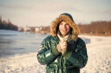 Sıcak ceketli, karlı bir arka plan. Rüzgara dayanıklı kıyafetler. Kışın elverişli hava koşulları. Güneşli kış günü. Kış erkek giyim. Kış kıyafeti. Hipster moda kıyafeti. Kapüşonlu adam.