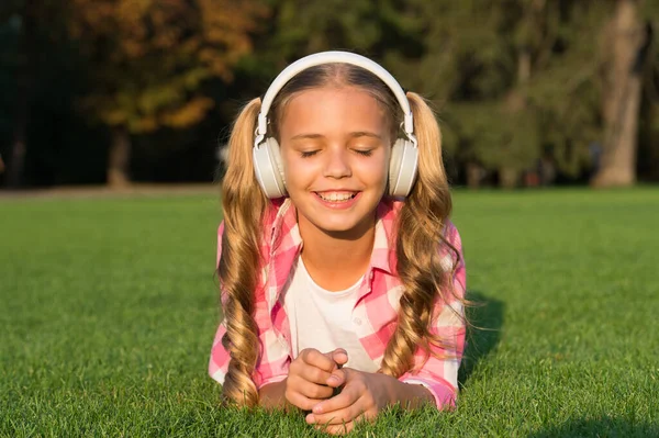 Happy girl dziecko z zamkniętymi oczami słuchać muzyki w słuchawkach relaks na zielonej trawie słoneczne lato na świeżym powietrzu, dźwięk — Zdjęcie stockowe