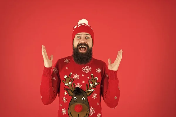 З новорічною концепцією. Приєднуйтесь до зимової святкової вечірки. Різдвяний светр вечірка. Зимове вбрання. Веселі заходи та речі. Хіпстер емоційний бородатий чоловік носить зимовий светр і капелюх червоний фон — стокове фото